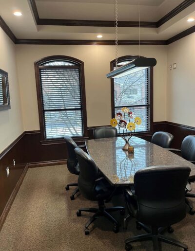 A conference room with a granite table, black office chairs, and a hanging rectangular light fixture.