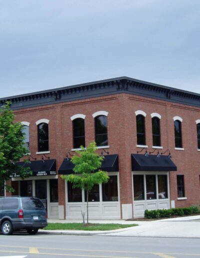 Two-story brick building with arched windows on the second floor, hosting a cafe and shops on the ground level, under a clear sky.
