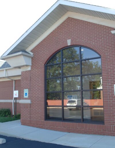 Brick commercial building with large arched windows and designated curbside pickup parking spaces.